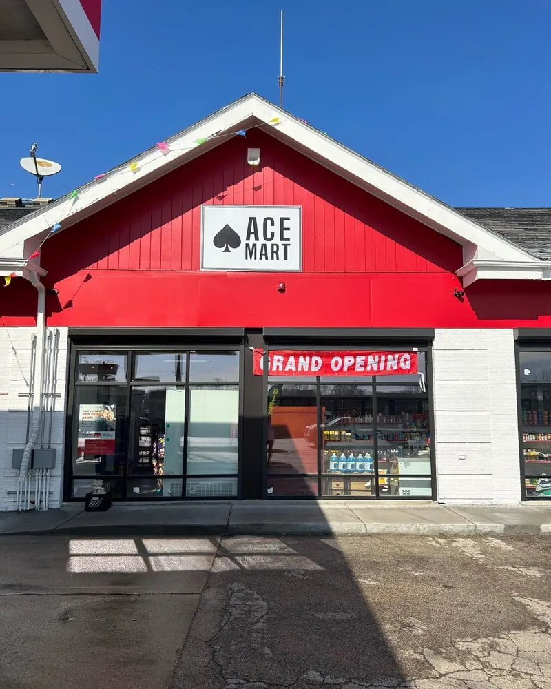 Red storefront with the Ace Mart sign in the gable and a Grand Opening banner over the door