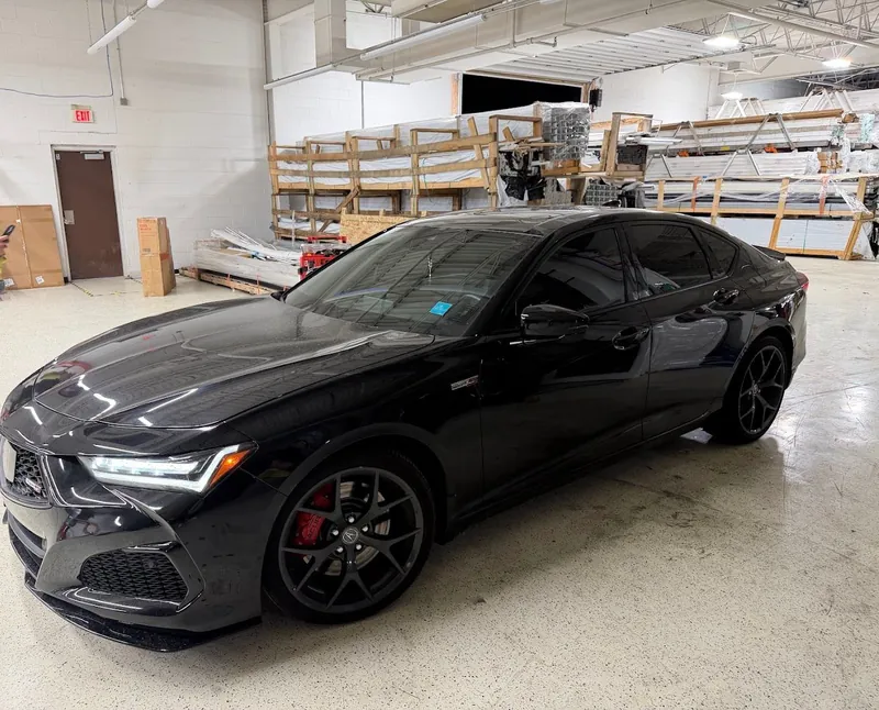 Black Acura sedan with red brake calipers and tinted windows in the shop