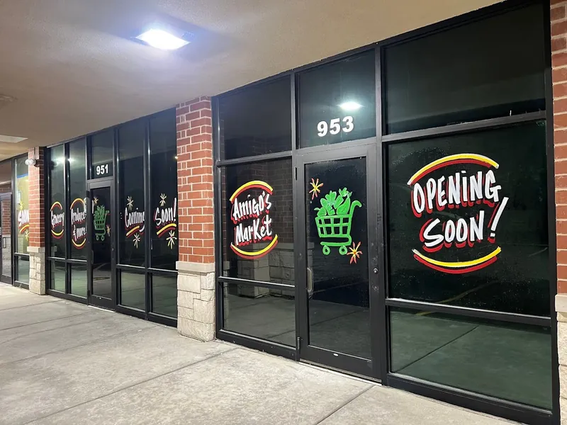 Storefront windows at night with Amigo's Market logos, a green shopping cart and Opening Soon lettering