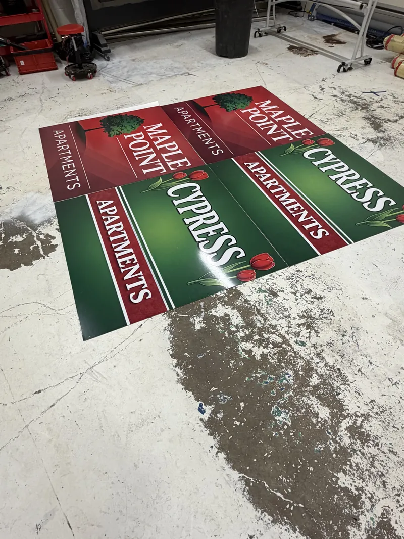 Red and green printed sign panels for Maple Point Apartments and Cypress Apartments laid out on a shop floor