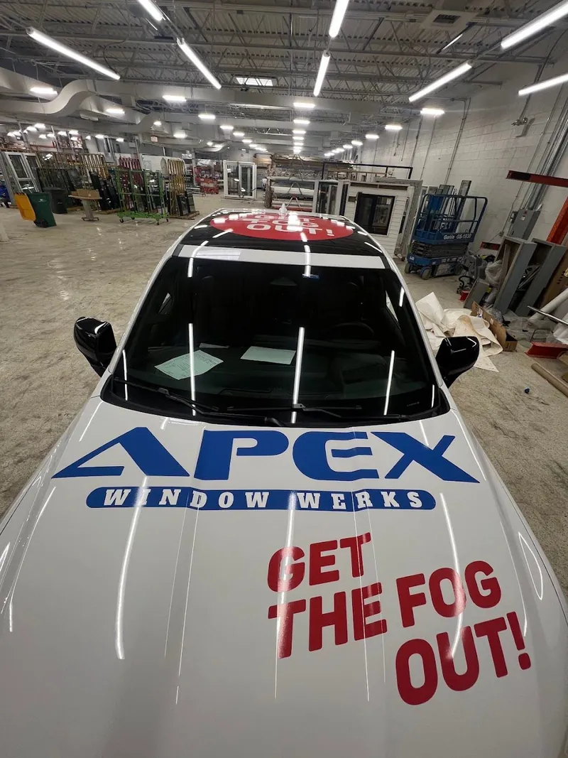 Hood of a white pickup with a blue APEX Window Werks logo and red Get the Fog Out lettering
