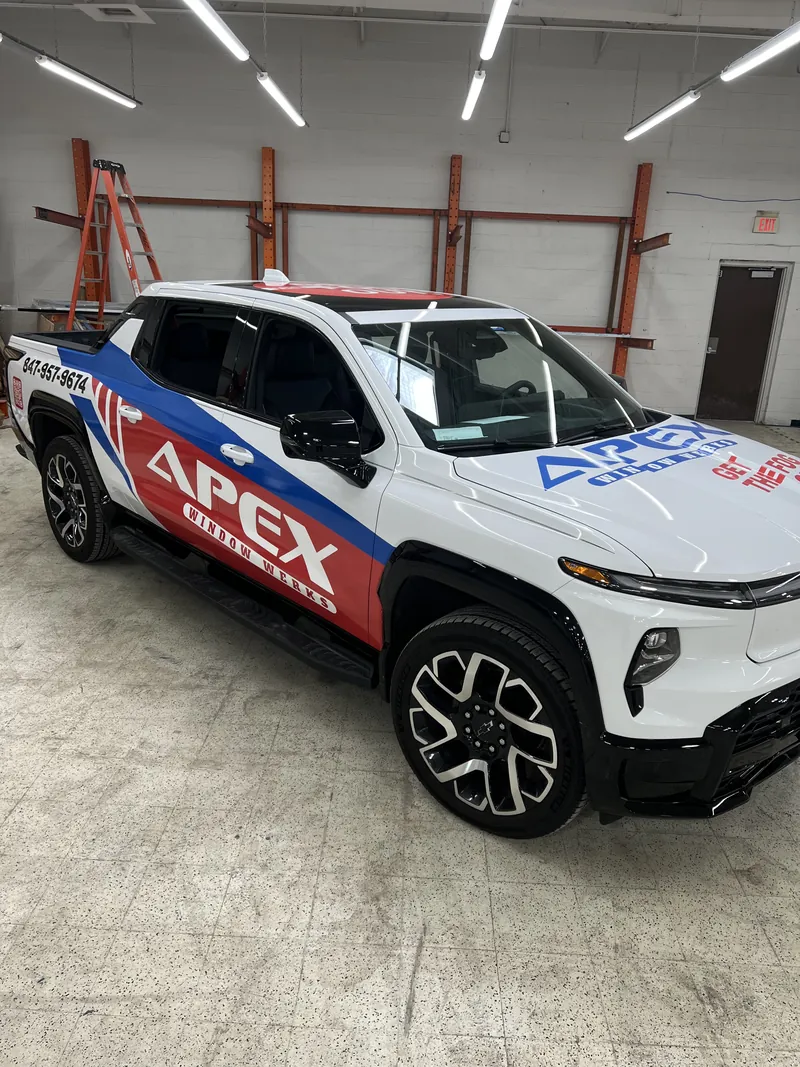 White pickup truck with a red, white and blue APEX partial wrap parked inside a shop