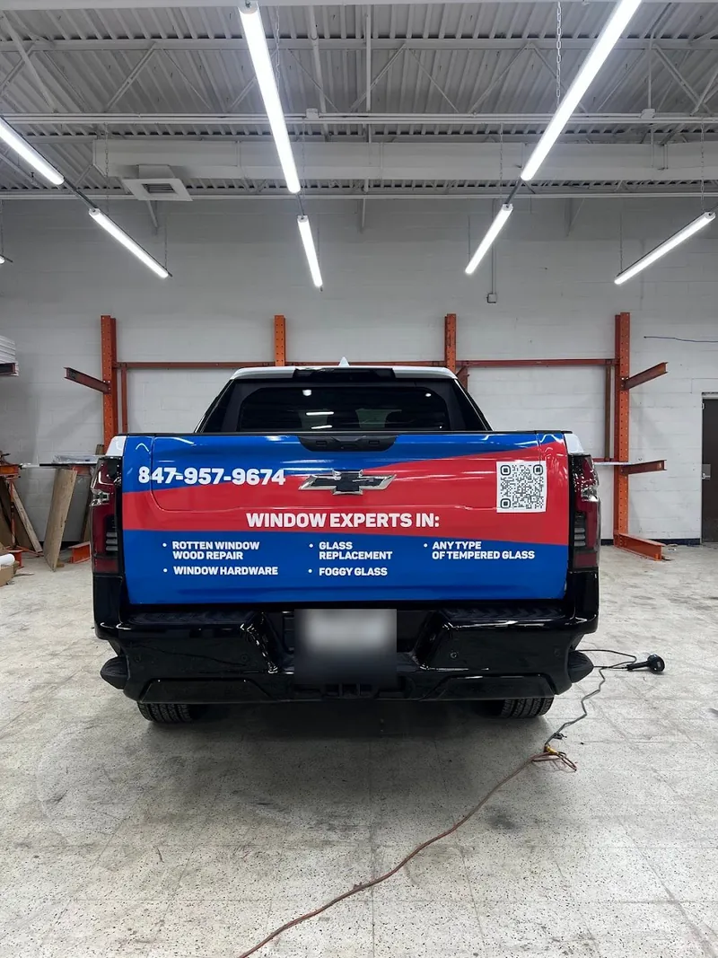 Rear of a pickup with red and blue tailgate graphics listing window services, a phone number and a QR code