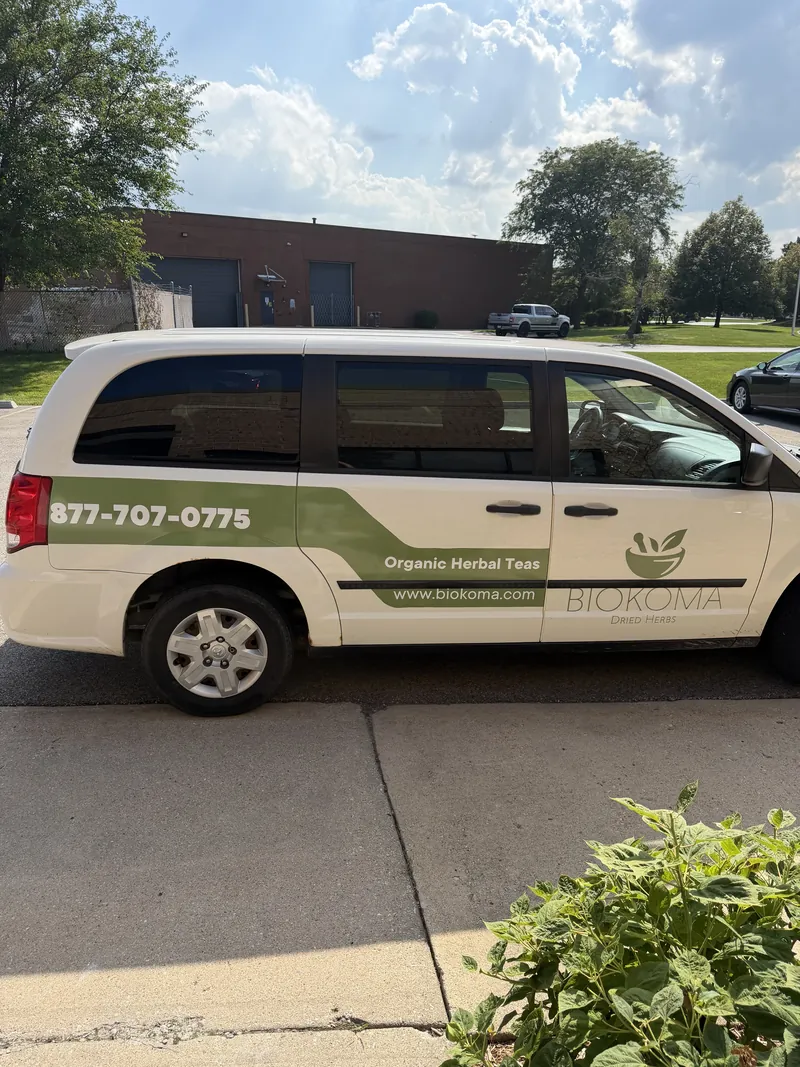 White minivan with green Biokoma organic herbal teas graphics, phone number and website on the side