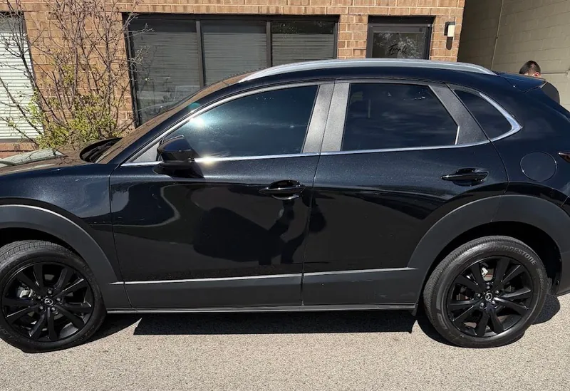 Black Mazda crossover with tinted windows parked outside a brick building