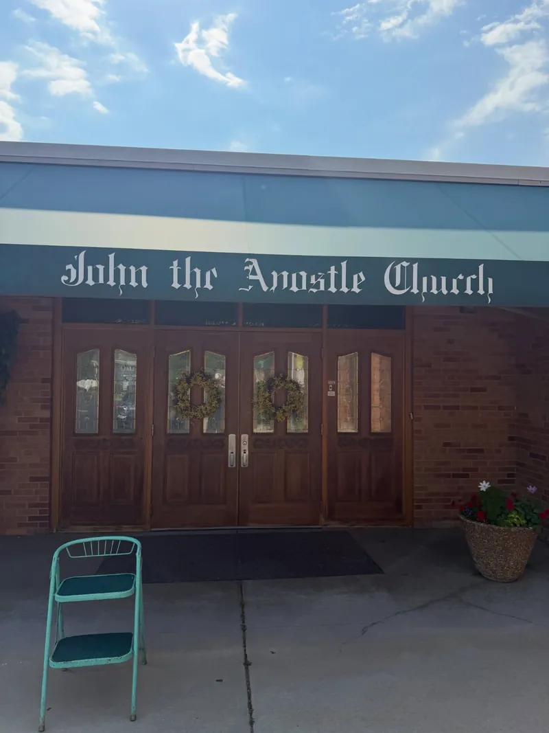 Gothic-style lettering reading John the Apostle Church on a fascia above wooden church doors