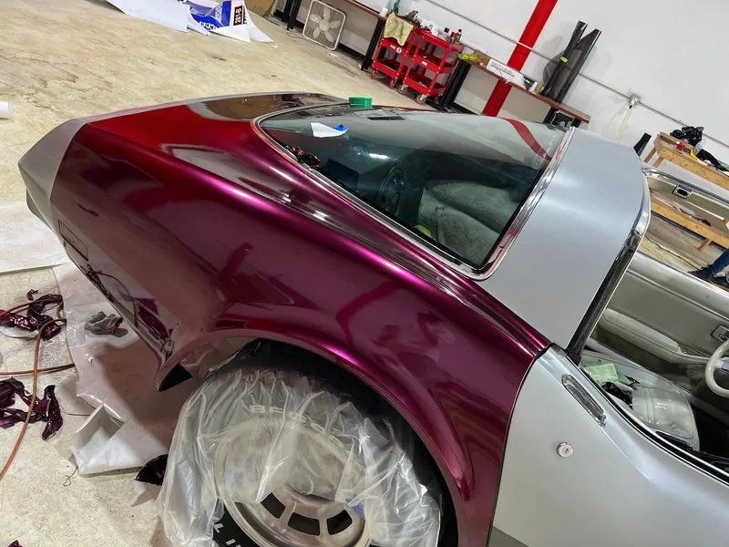 Candy red vinyl being applied over the silver paint of a classic Corvette in the shop
