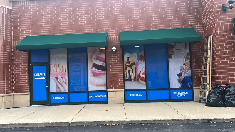 Two storefront windows under green awnings covered in blue printed dental window graphics
