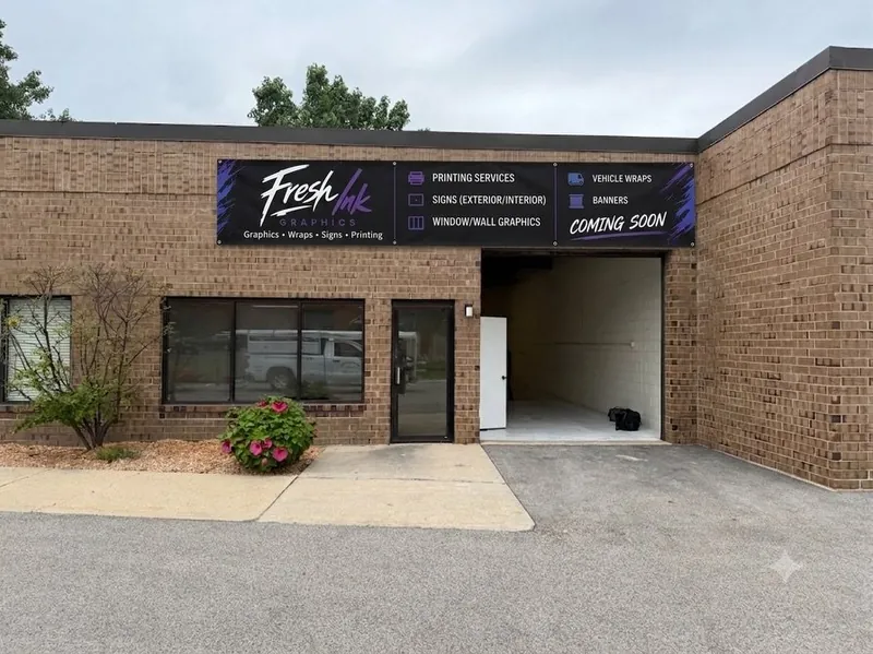 Brick building with a Fresh Ink Graphics banner sign listing printing, signs, window and wall graphics, vehicle wraps and banners, marked Coming Soon