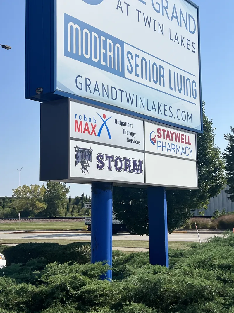 Blue and white pylon sign for The Grand at Twin Lakes with tenant panels for Rehab Max, Staywell Pharmacy and Storm