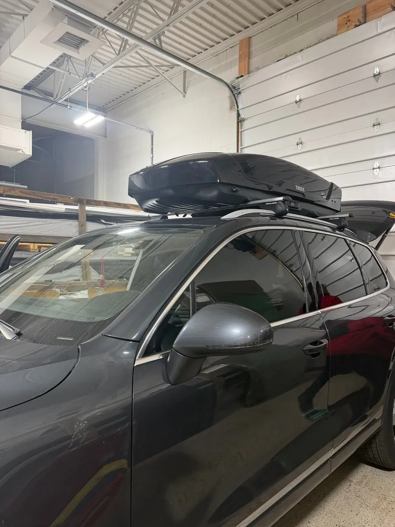 Dark gray wagon with a roof cargo box and freshly tinted windows inside the shop