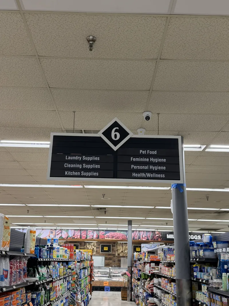 Numbered black aisle directory sign listing product categories, hanging above grocery shelves