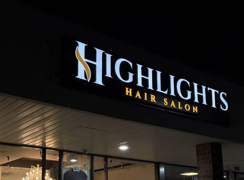 Highlights Hair Salon storefront sign lit at night, white channel letters with gold accent lettering