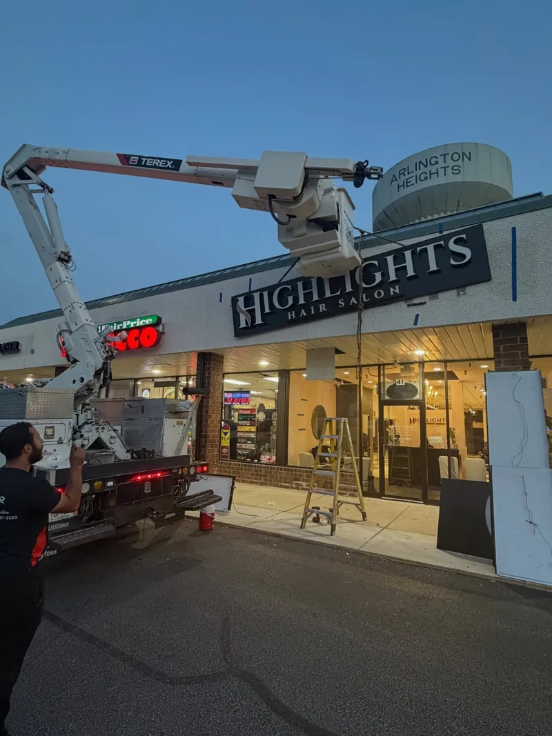 Bucket truck raised at dusk while the Highlights Hair Salon sign is mounted on a strip-mall façade