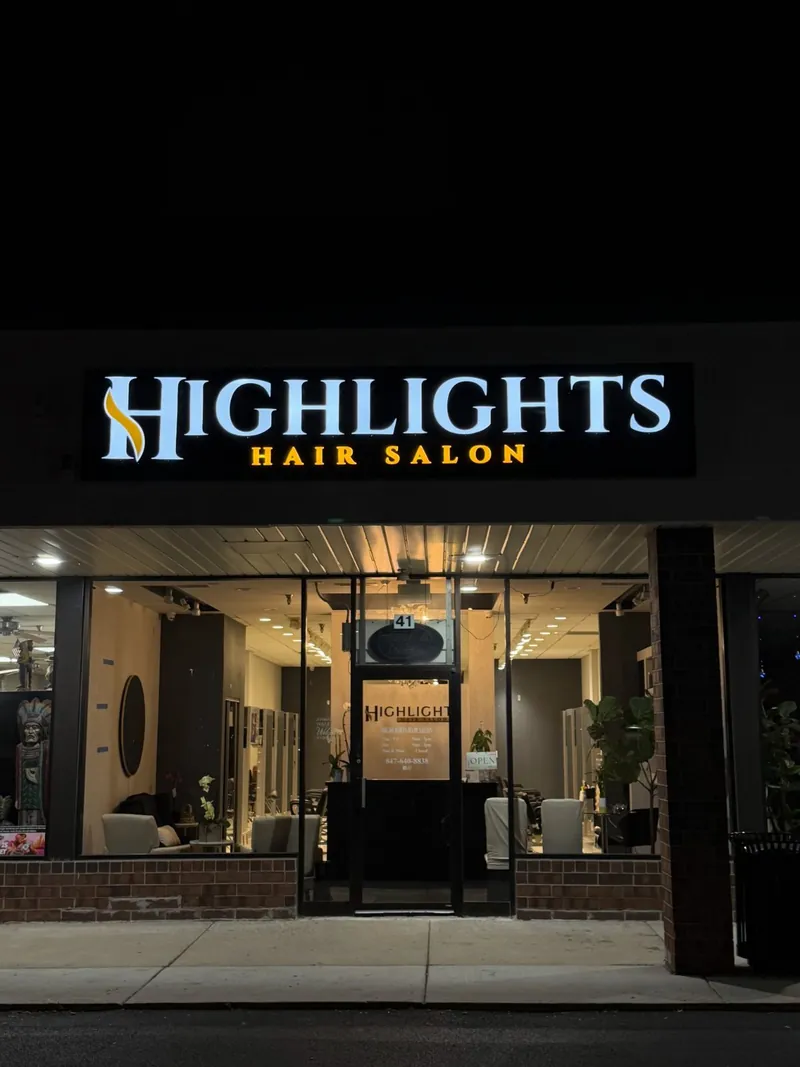 Straight-on night view of the illuminated Highlights Hair Salon sign above a lit salon storefront