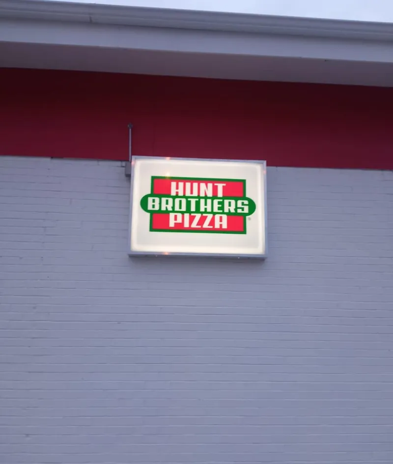 Lit Hunt Brothers Pizza sign mounted on a gray brick store wall