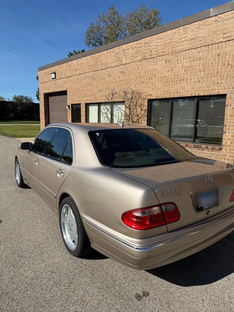 Champagne Mercedes-Benz sedan with a tinted rear window, parked outside a brick building
