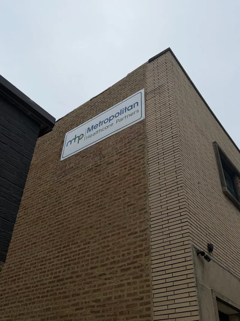Brick building corner with a white Metropolitan Healthcare Partners sign under an overcast sky