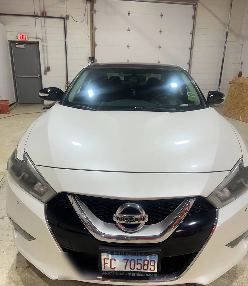 Front of a white Nissan Maxima with its chrome grille trim wrapped in gloss black