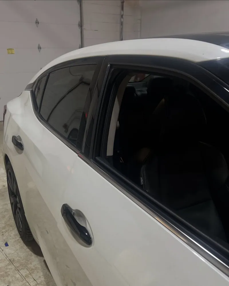 Side window trim of a white Nissan Maxima wrapped in gloss black