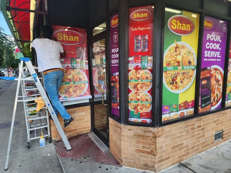 Installer on a ladder applying colorful Shan food graphics to a corner storefront's windows