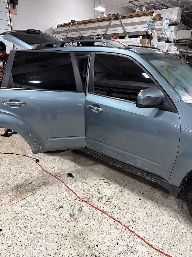 Blue-gray SUV with its doors open in the shop during a window tint job