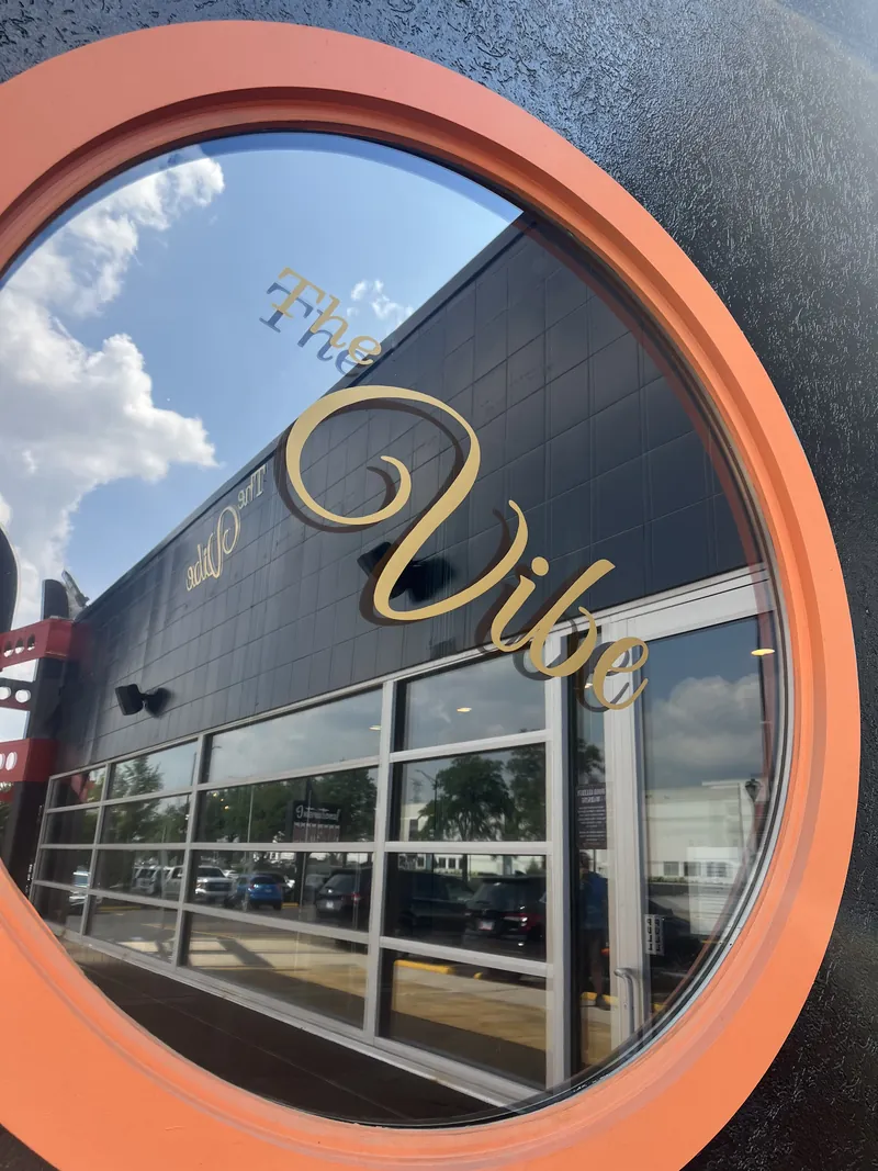 Gold script dimensional letters spelling The Vibe on a dark building façade, framed through a round orange portal