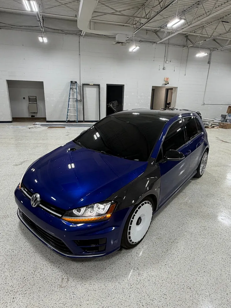 Blue Volkswagen Golf R hatchback with tinted windows on the shop floor
