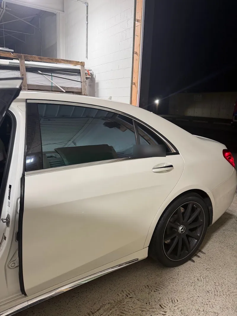 White Mercedes-Benz sedan with tinted windows and a door open in the shop